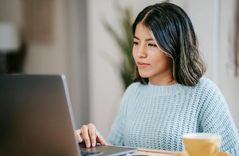A female student using a laptop near a tea mug in a room