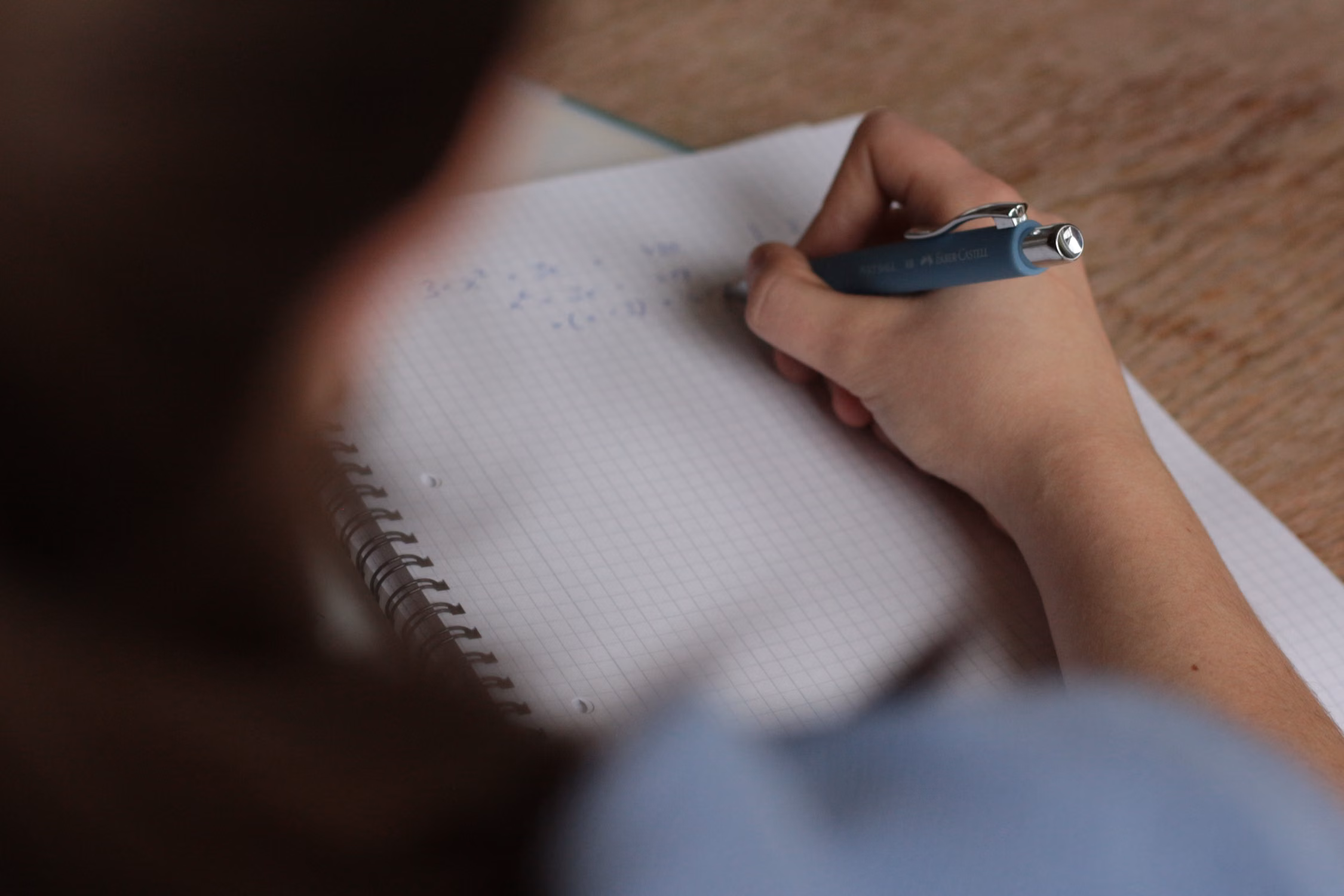 A person writing on paper, likely working on a test