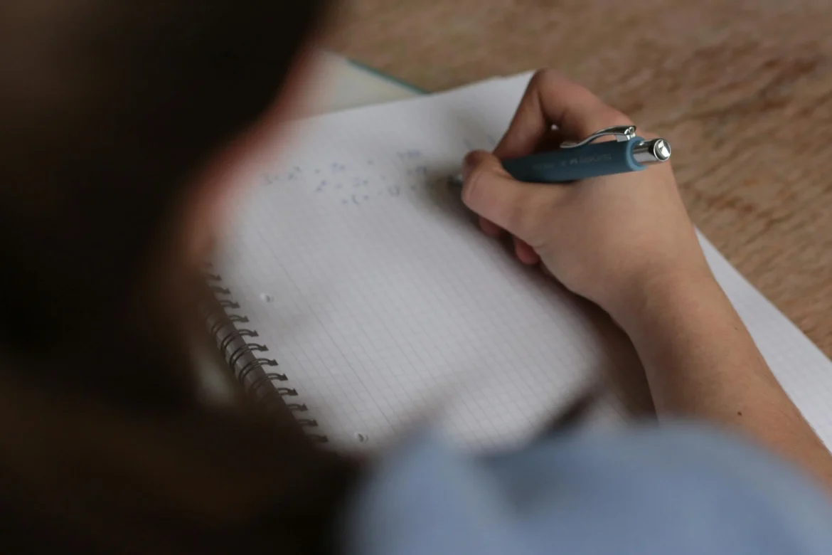 A person writing on a paper, likely working on a test