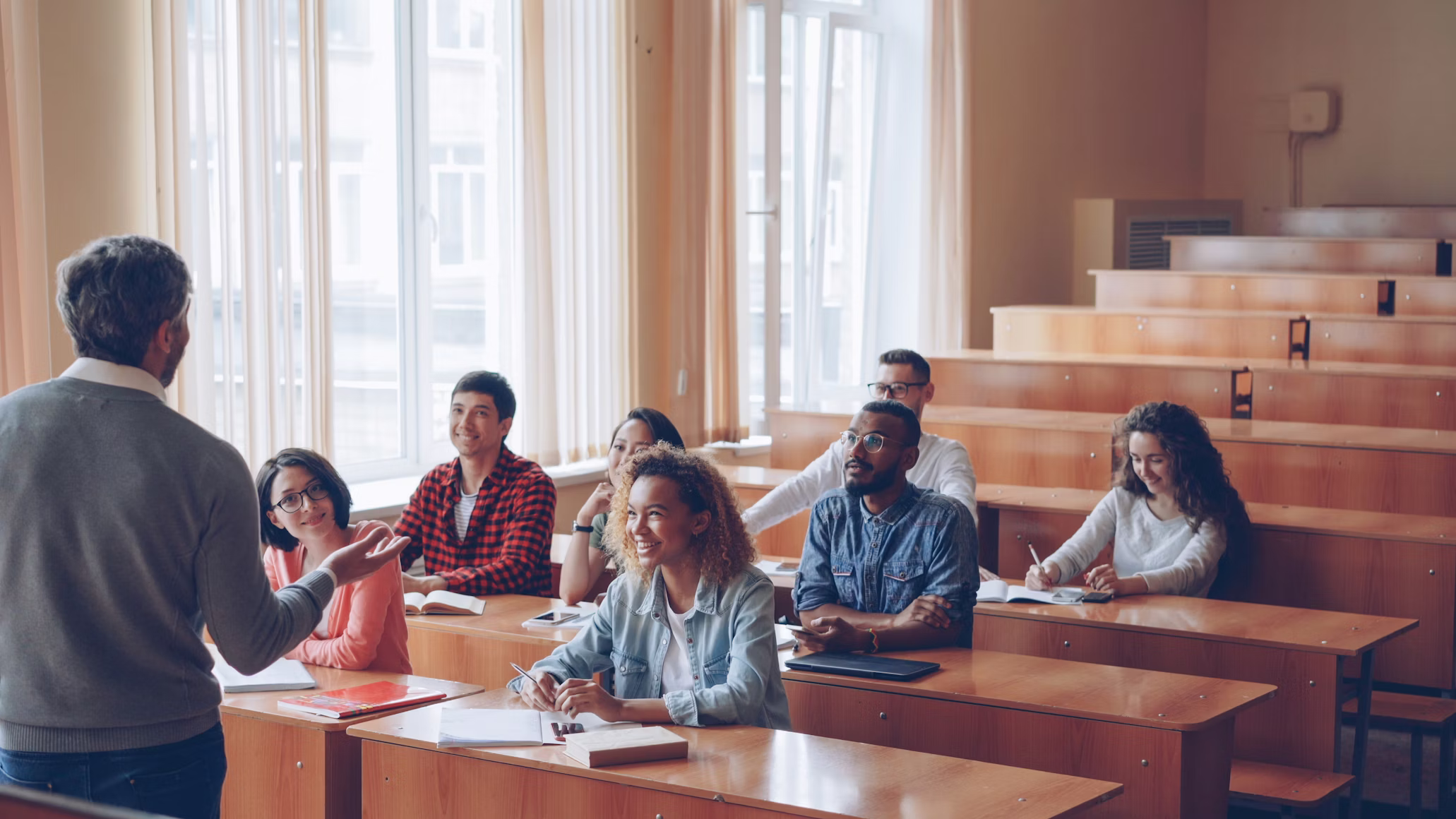 A professor lecturing a diverse group of college students in a bright university lecture hall.